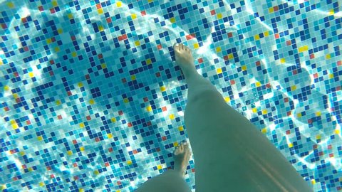 Female legs walking along bottom of pool. Point of view of woman stepping at swimming pool during summer vacation. POV Close up Slow motion