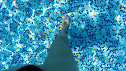 Male legs walking along bottom of pool. Point of view of man stepping at swimming pool during summer vacation. POV Close up Slow motion