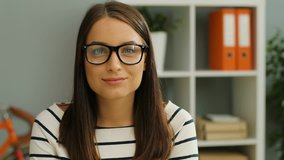 Close up of a charming young woman in glasses smiling straight into the camera. The blurred office background. Indoor. Portrait