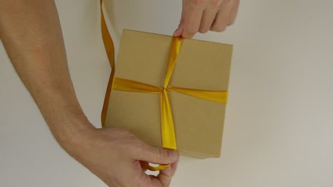 Preparing for a gift giving gift. Gift box packing with gold ribbon. Hands wrap the gift box with a yellow ribbon and make a bow. Close up top view high angle.