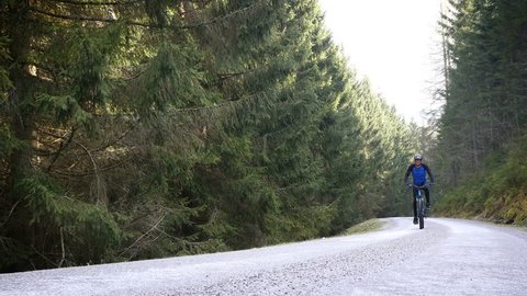 Man riding E-bike uphill on forest road 