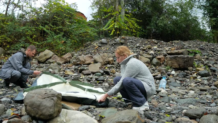4k. guy and girl tourist collects a tent on the bank of a mountain river