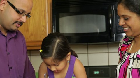 Dad and mom supervise their little daughter who is trying to scoop frozen ice cream out of a container.: film stockowy