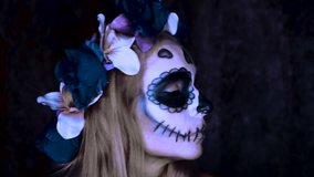Closeup face of woman with Mexican sugar skull makeup and flowery wreath looking into the camera and sending air kiss. Creative, artistic, Halloween concept - slow motion video