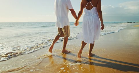Happy romantic couple walking down the beach at sunset
