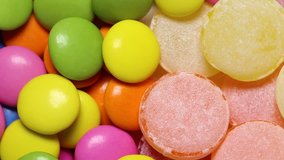 Macro video of many tasty round candies isolated on white background. MIx of bright yellow, orange, green, pink and blue sweets rotating. Real time full hd video clip.