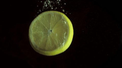 Round fresh juicy lemon slice plunging into transparent water with explosive stunning splash, breaking the surface of liquid. Underwater high-speed slow motion shot on black background isolated.