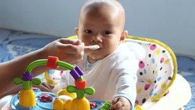 Cute little baby asian feeding with a spoon at the table, boy eating solid foods.4k video