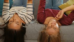 Young women listening to the music and lying on the couch upside down. Friends having fun at home. Inside