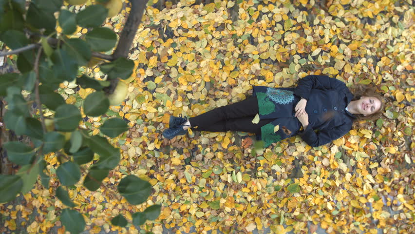 The girl among the yellow leafs. Slow motion. Top view. A young cheerful girl lies on the leaves. She looks on the up and smiles. The camera moves smoothly over the girl from left to right.