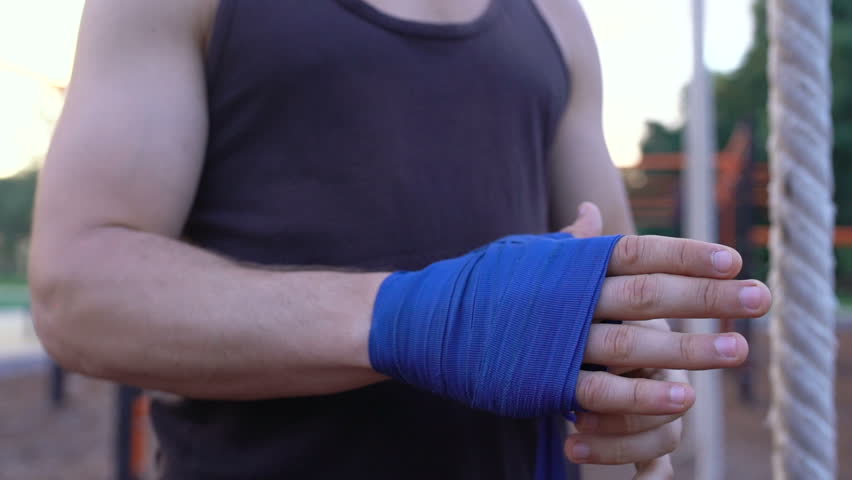 Strong kickboxing man putting on punching wraps and get his palm in fist.