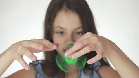 Beautiful cheerful teen girl playing with green fidget spinner on a white background stock footage video