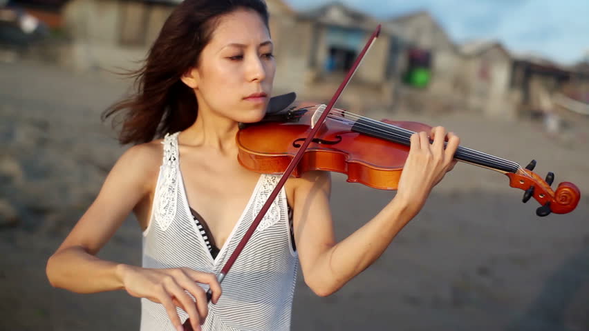 young girl playing on violin standing on the beach