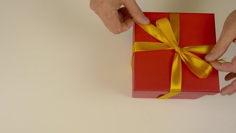 Big unpacked red gift box with gold ribbon. Hands untie the ribbon of a golden ribbon on a red gift box. Top view high angle. Close up.