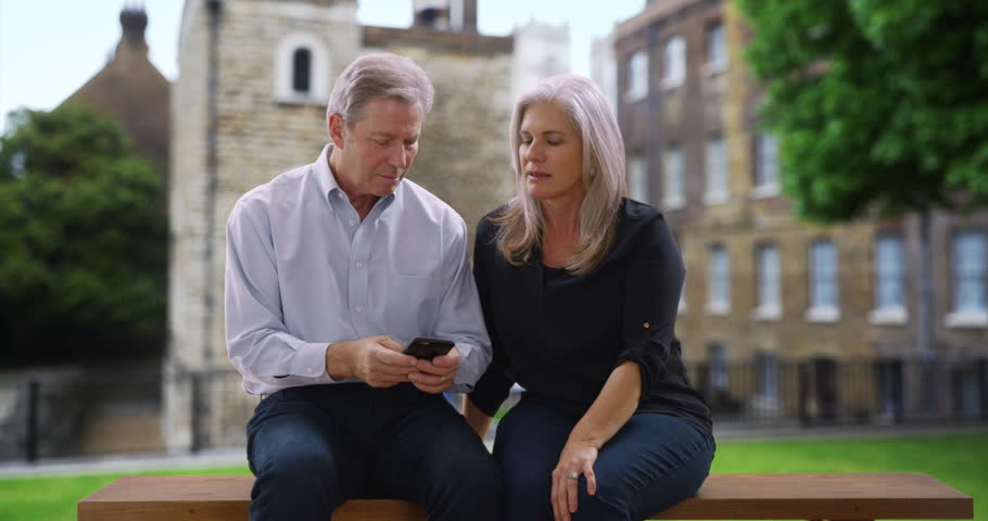 Senior white couple sitting on bench in London have a chat about a recent event. Old man and woman have a conversation about an interesting thing that happened outside in London, England. 4k