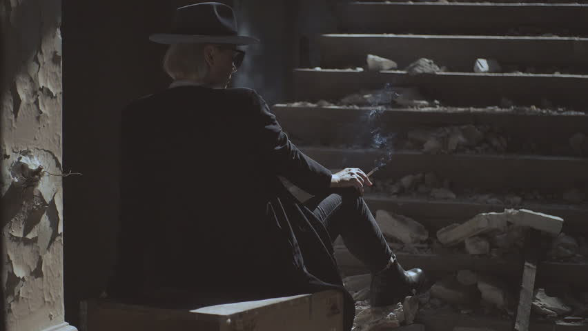 A beautiful girl in black clothes and a hat, walking along an old collapsed building. The girl in a hat smokes