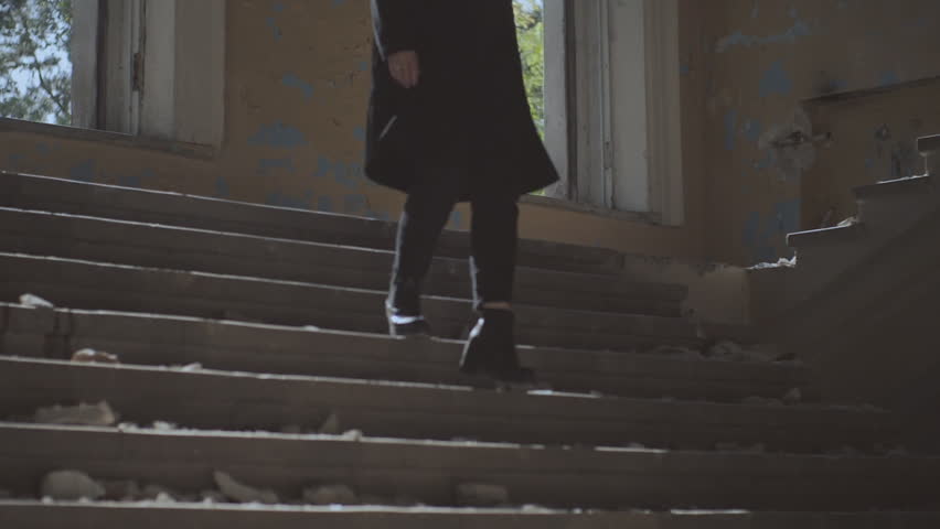 a girl in black clothes and wearing a hat. The girl goes down the steps in the ruined building