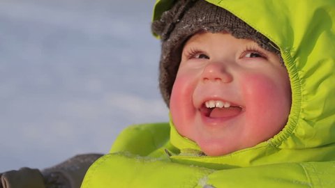 Close-up of face pink-cheeked smiling baby winter outdoor in snowy sunny weather
