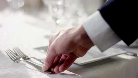 Shot of waiter hand correcting cultery on table before celebration at banquet hall