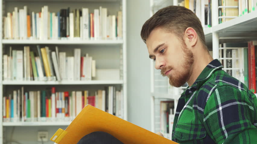 A laughing guy is sitting in the library and reading