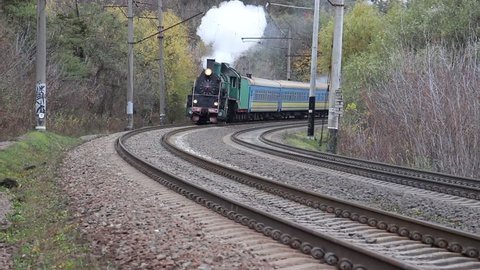 A steam locomotive moving forward and signaling with a steam whistle.