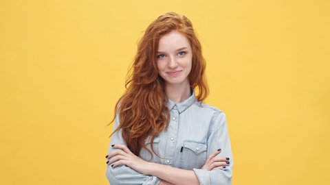 Smiling mystery ginger woman in denim shirt holding crossed arms and looking at the camera over yellow background
