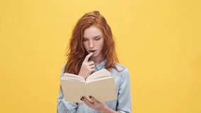 Serious ginger woman in denim shirt reading book while interfere her over yellow background