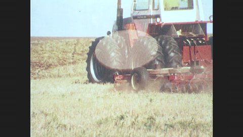 1970s: Tractor driving. Men with machinery. Man pours seed. Hands put down can, pick up beaker of liquid. Plane sprays field. Man looks at wheat. Combine harvesting wheat.