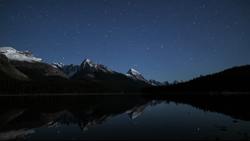 An night timelapse at Maligne Lake in Jasper National Park, Alberta, Canada. Reflections of shooting stars across the top of Leah, Samson Peaks and surrounding snowcapped mountains. A winter scene. 