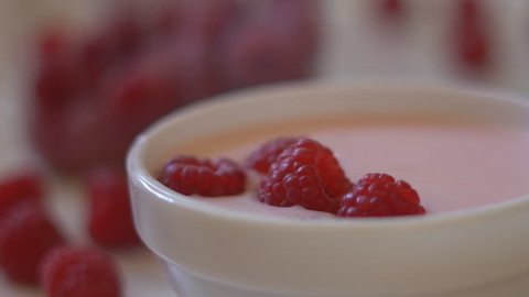 large juicy berries of raspberries fall in a plate with white yogurt. delayed shooting. large salt berries are appetizing.