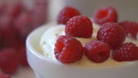 large juicy berries of raspberries fall in a plate with white yogurt. delayed shooting. large salty berry appetizingly lie on the surface. A small teaspoon slowly raises and lowers fresh berries. a