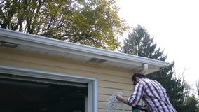 Caucasian Millennial husband frustrated at hanging icicle lights for Christmas time on ladder