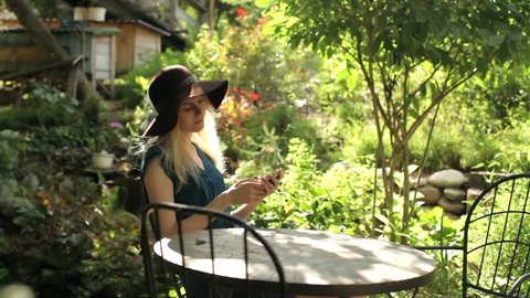 beautiful girl with a phone at a cafe table in the garden