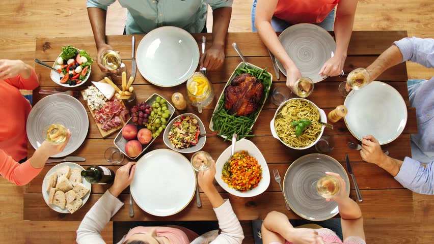 Eating and holidays concept - group of people at table with food clinking wine glasses