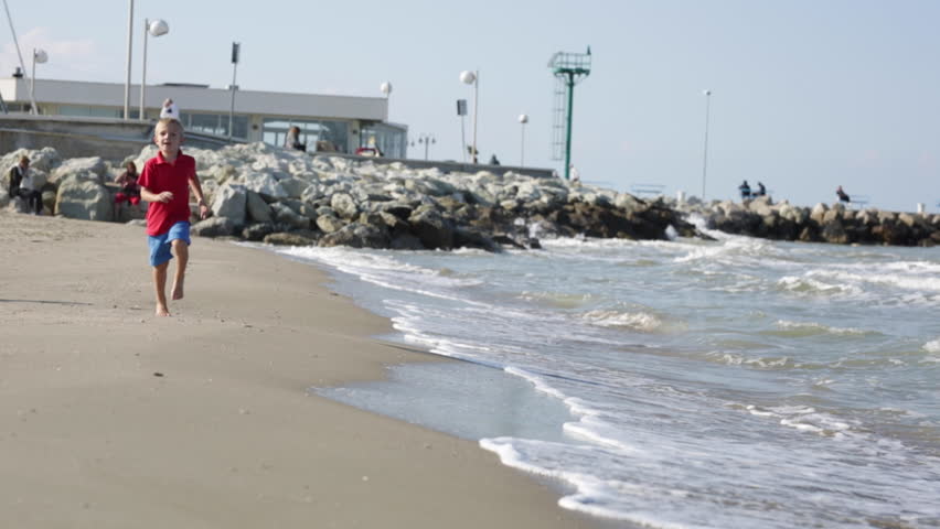 Happy smiling little boy running at the beach near the sea