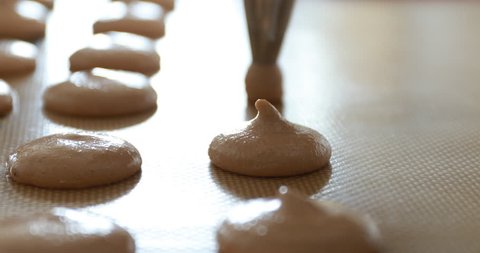 Making caramel macaroon : hand laying out caramel macaroon dough on tray for baking using pastry bag