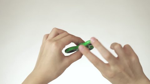Hands of a teenage girl spin a green fidget spinner on a white background stock footage video