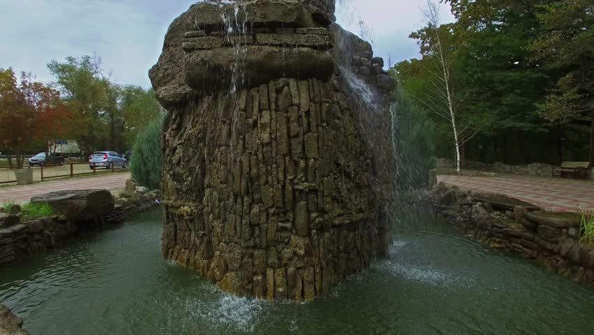 Fountain made from big rocks on small square among plants at autumn day. Aerial view