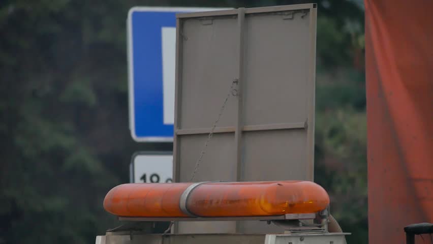 Rotating beacon of the vehicle as a sign of road works. Dust rising into the air. Flashing light. Workers with air compressor cleaning street before paving. Street repair, road reconstruction.