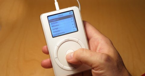 Circa November, 2017 - A user scrolls through music and settings on an old iPod 2nd Generation. The iPod is a popular MP3 player first introduced by Apple in 2001.  	