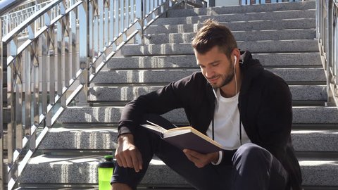 The calm guy is reading a book sitting on the steps