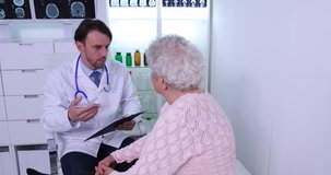 Medical Doctor Man Writing Notes on Clipboard and Talking with Old Patient Woman