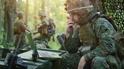 Military Staging Base, Chief Army Engineer/ Signalman Uses Walkie-Talkie Radio and Army Grade Laptop. Squads Resides in Camouflaged Tent While Being on Reconnaissance Operation/ Mission. 4K UHD.