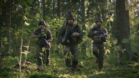 Three Fully Equipped Soldiers Wearing Camouflage Uniform Attacking Enemy, They're in Shooting Ready Stance, Aiming Rifles. Military Operation in Action, Squad Standing in Dense Forest. 4K UHD.