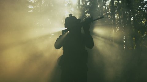 Silhouette of the Fully Equipped Soldier Moving Through Smokey Forest with Rifle Ready To Shoot. Reconnaissance Military Operation. Shot on RED EPIC-W 8K Helium Cinema Camera.