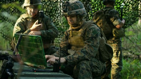 Military Staging Base, Officer Gives Orders to Chief Engineer, They Use Radio and Army Grade Laptop. They're in Camouflaged Tent in a Forest. They're on Reconnaissance Operation Mission. 4K UHD.