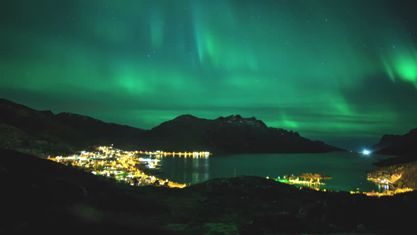 Time lapse of a northern light in northern Norway. Calm fjord and a seashore village