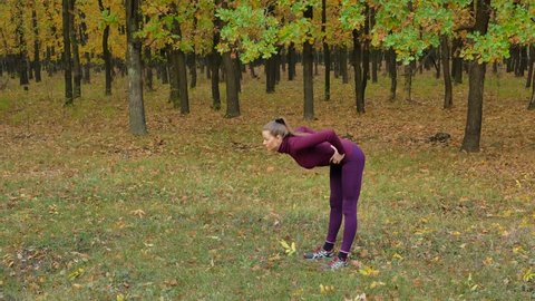 Beautiful fitness sport girl does warm up before running in autumn park. Workout outdoors.