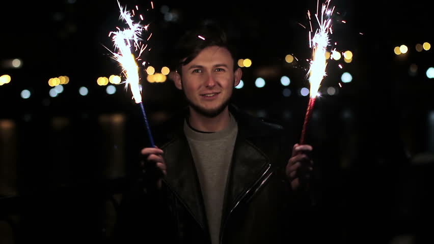 A cheerful young guy with fireworks in his hands. He dances and jumps with happiness