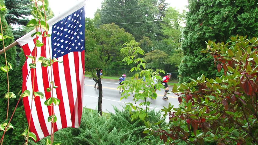 American flag waves in wind as inline skaters race in street marathon.